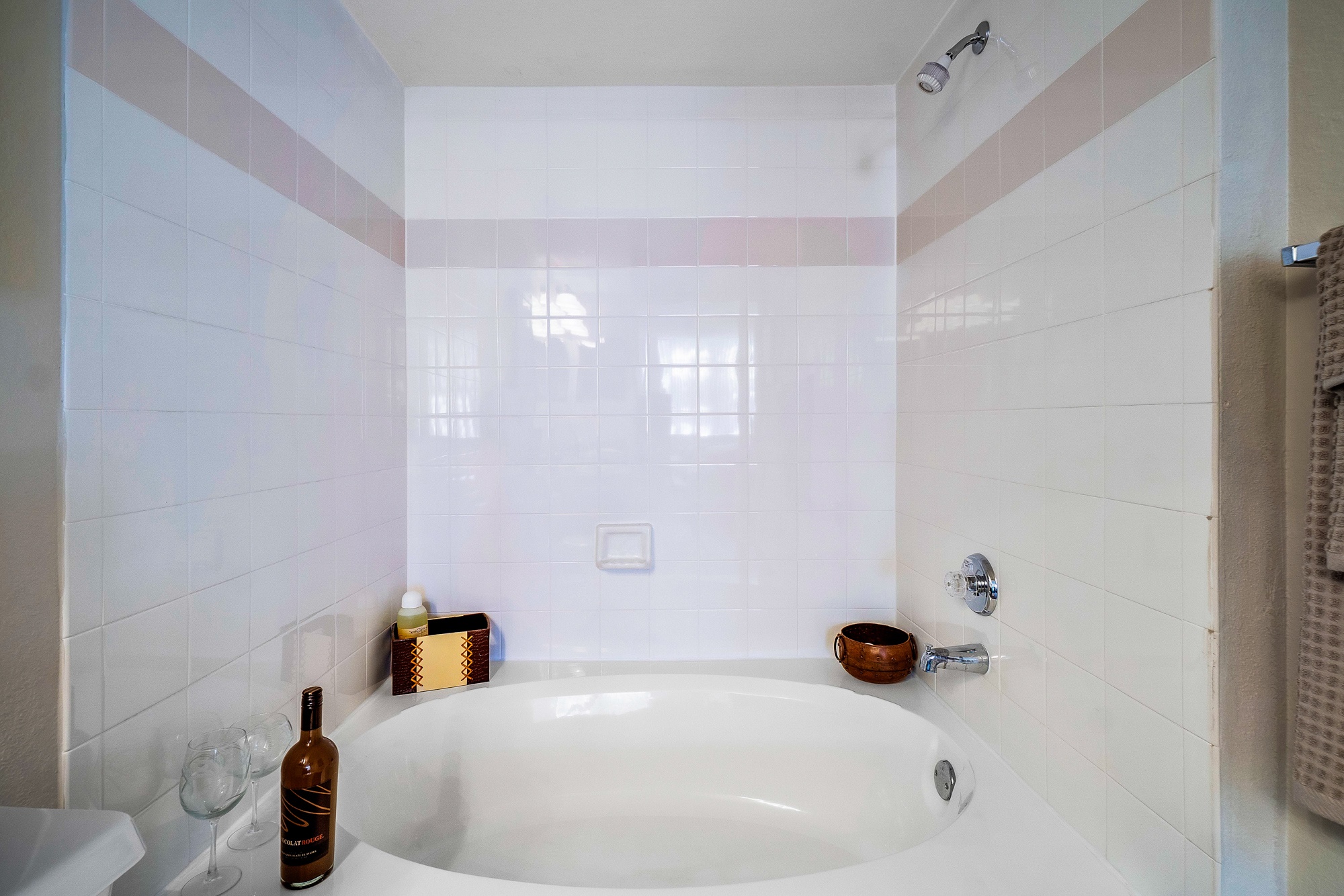 A white bathroom with a white tub and a bottle of wine.